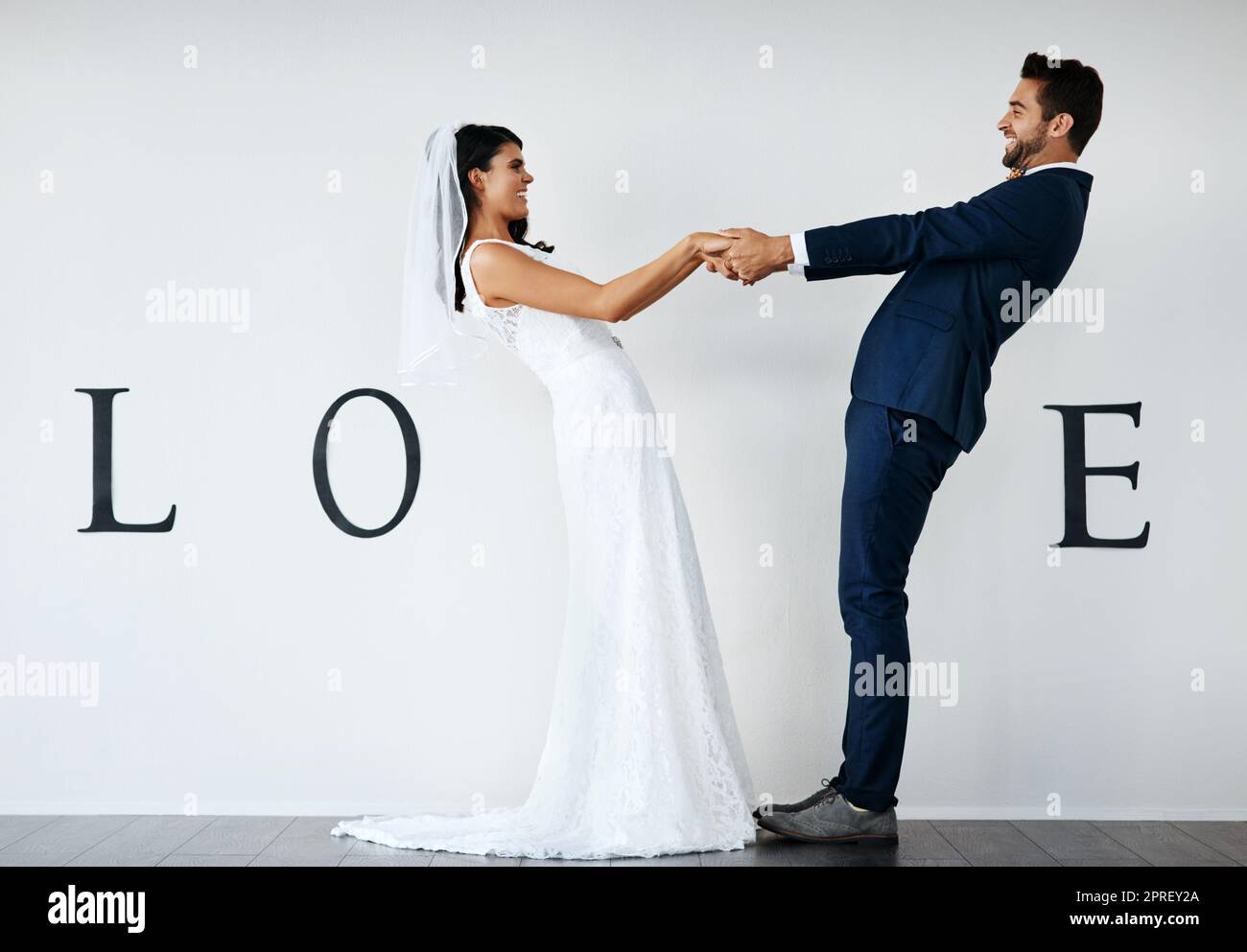Love spins you around. Concept studio shot of a bride and groom making an V in the word love against a wall. Stock Photo