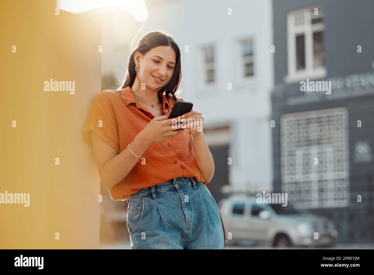 Texting on a phone, waiting for public transport and commuting in the city with a young female tourist enjoying travel and sightseeing. Looking online for places to see and visit while on holiday Stock Photo