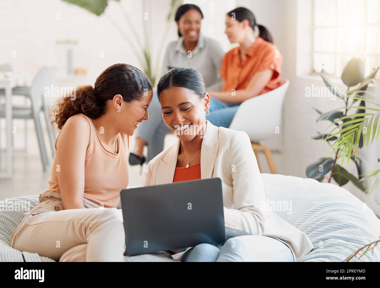 Group of business women on a laptop sitting, laughing looking at social media during a break. Happy ladies bonding on a couch at work. Excited team of girls celebrating new goal achieved at startup Stock Photo