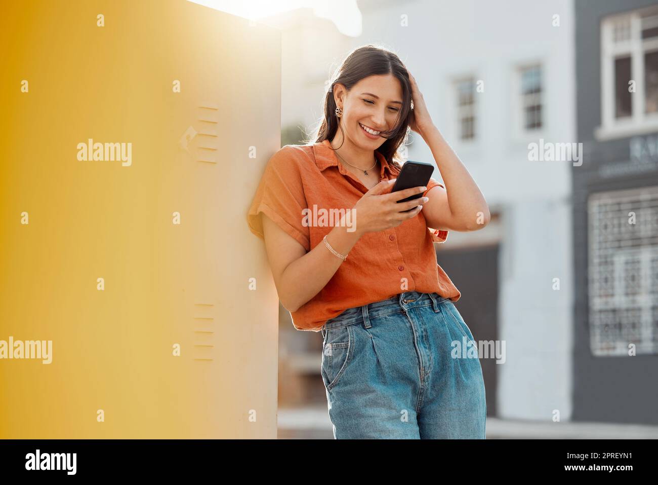Woman texting, browsing and scrolling on phone while chatting on social media, waiting for taxi and commuting in an urban city. Happy, trendy and smiling female tourist reading online notification Stock Photo
