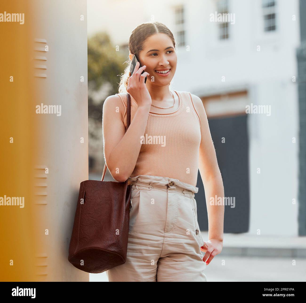 Casual woman talking on phone call, networking and making conversation while standing in the urban city alone. Trendy, smiling and cheerful female commuting and traveling to work in the morning Stock Photo