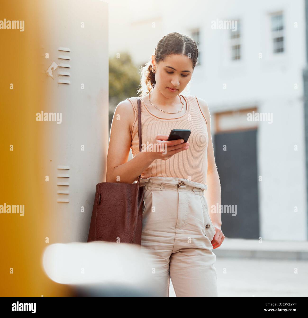 Traveling businesswoman with a phone texting, browsing internet while waiting outside for transport or replying to text while commuting to work. Young worker booking online transport service in city Stock Photo
