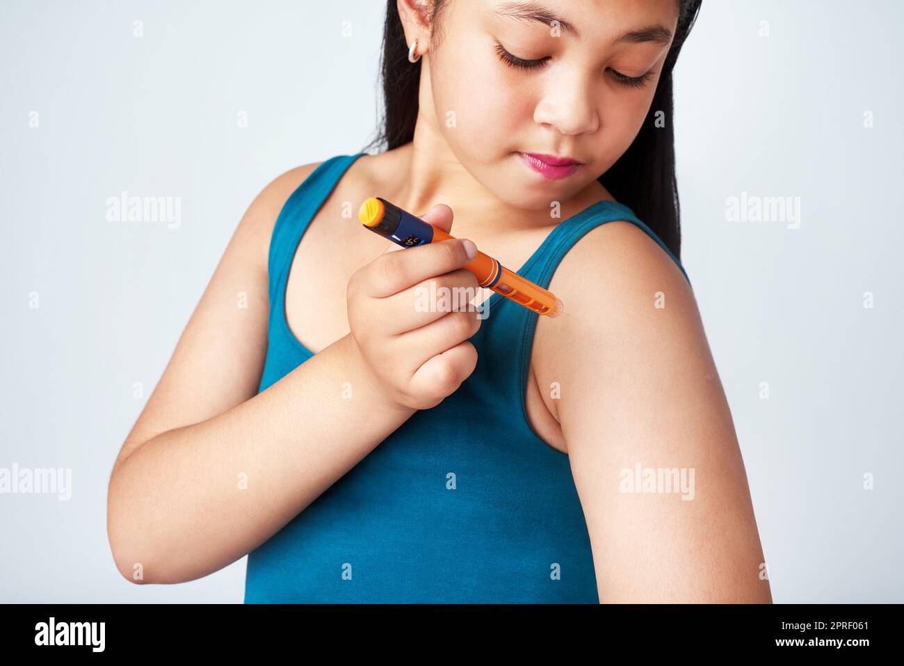 Keeping her diabetes under control. Studio shot of a cute young girl injecting herself with insulin shot against a gray background. Stock Photo
