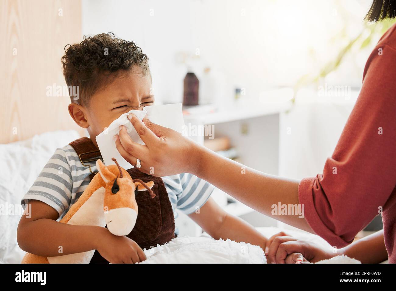 Flu, sick or cold child with parent sneezing, blowing and wiping runny nose while ill with covid virus, sinus and allergy symptoms in bed at home. Mother caring for stuffy and congested little son Stock Photo