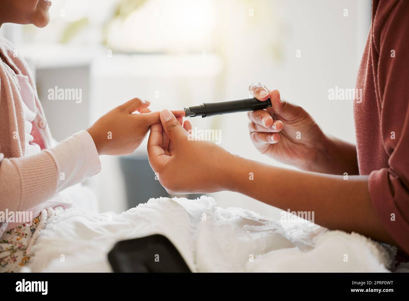 Diabetes, care and wellness by diabetic child being tested by her mother, monitoring her glucose at home. Parent using a blood sugar measuring device on her daughter, sticking to their daily routine Stock Photo