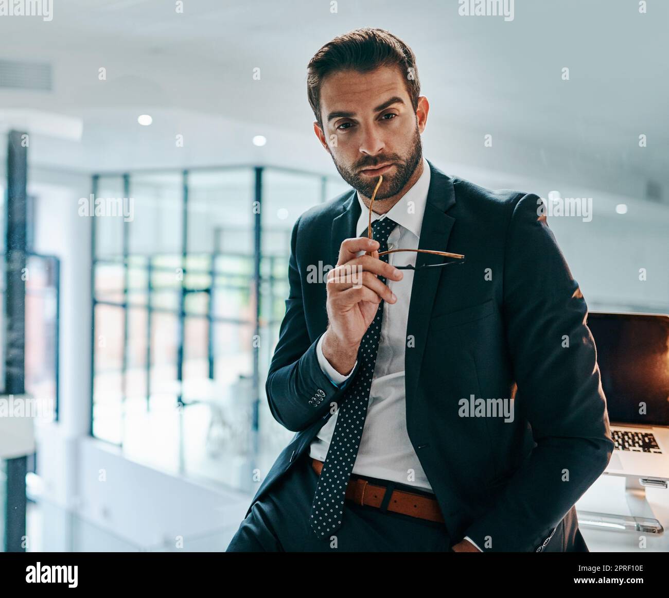 He has the looks that kill. Portrait of a confident young businessman leaning against his table inside of the office during the day. Stock Photo