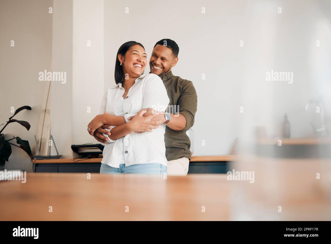 Hugging, romance and playful couple enjoying cuddle, love and bonding while laughing together at home. Loving husband giving affection, care and embrace to his happy, relaxing and funny wife Stock Photo