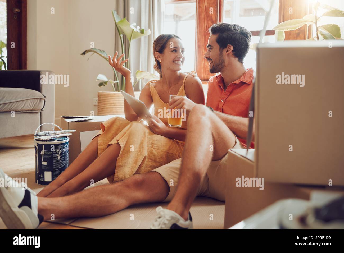 Home owner couple taking a break from painting, moving into new house or remodeling living room interior design. Husband, wife searching home improvement ideas online with tablet on a relaxing day Stock Photo