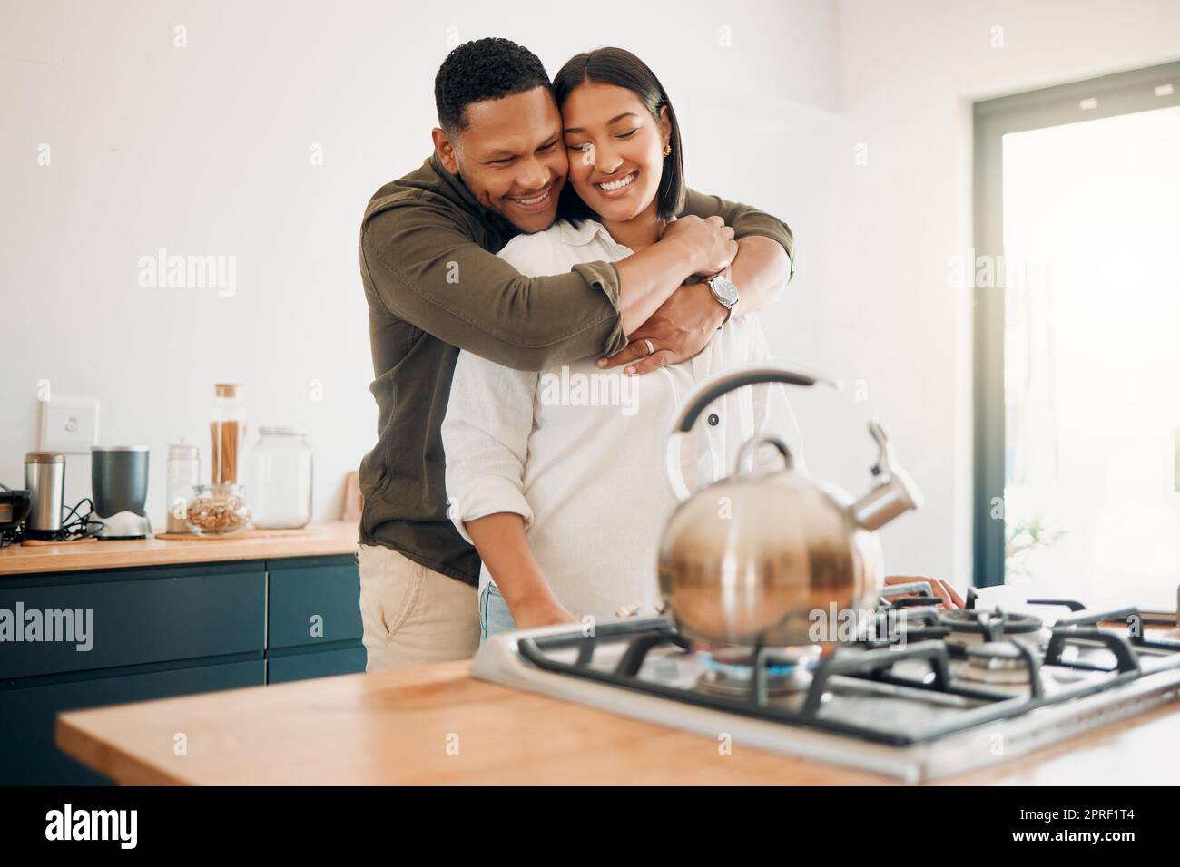 Romantic, love and bonding couple hugging while enjoying quality time together at home. Loving husband showing affection, care and embrace to his relaxing wife while making tea in the kitchen Stock Photo