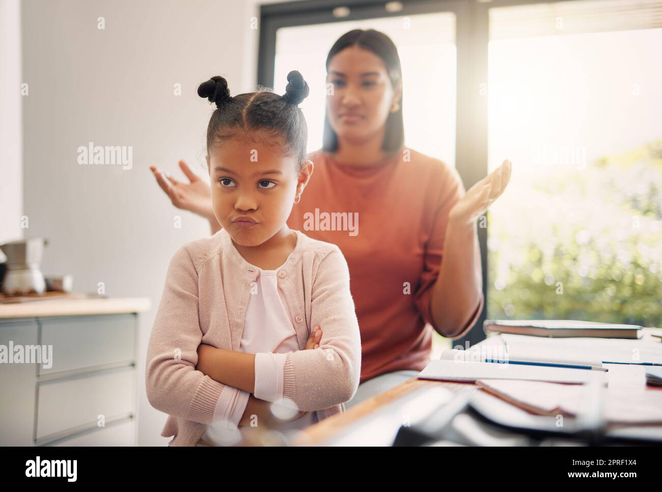 Upset, discipline and family while offended and stubborn little girl looking unhappy with her scolding mother in the background. Naughty, problem and bad child angry and ignoring her parent at home Stock Photo