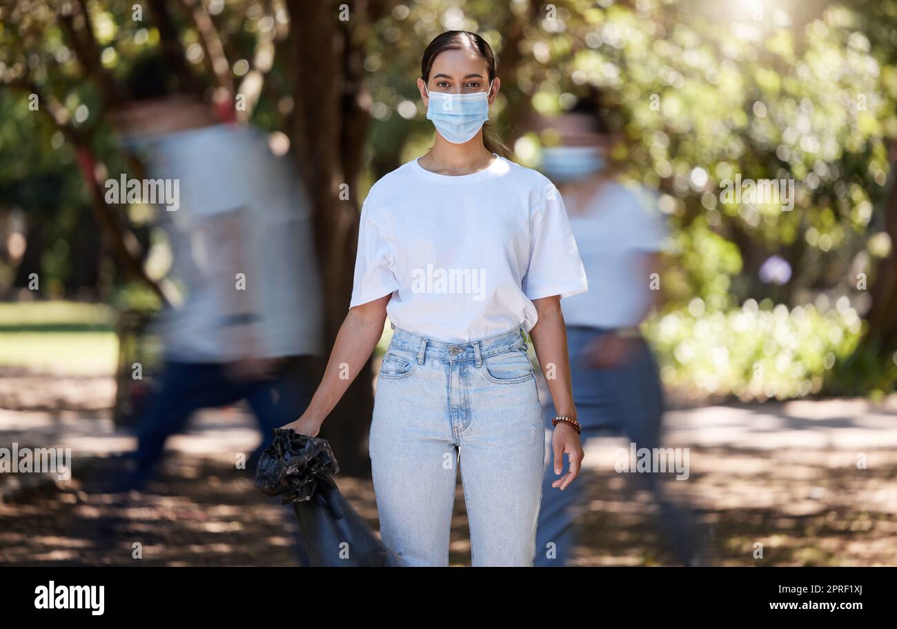 Woman in covid face mask cleaning the park for clean, hygiene and safe green environment. Responsible activist, volunteer or community service worker with rubbish, trash and garbage in a plastic bag Stock Photo