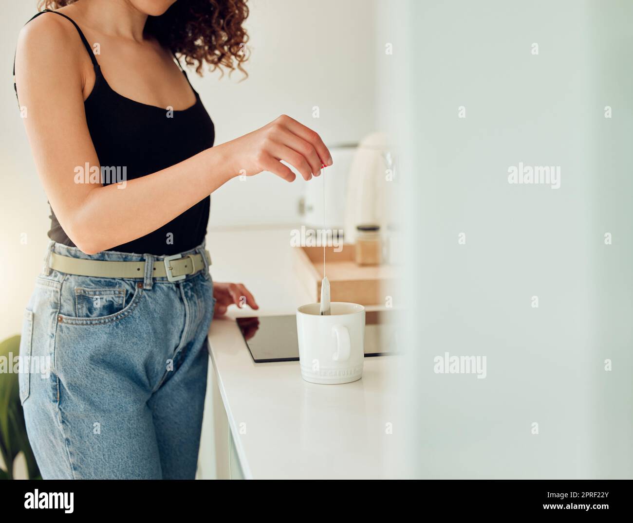 Woman hand holding herbal tea bag over cup of boiling water, making chai in kitchen taking a break. Female barista woman working at cafe or coffee shop counter, hot drink during office lunch break. Stock Photo