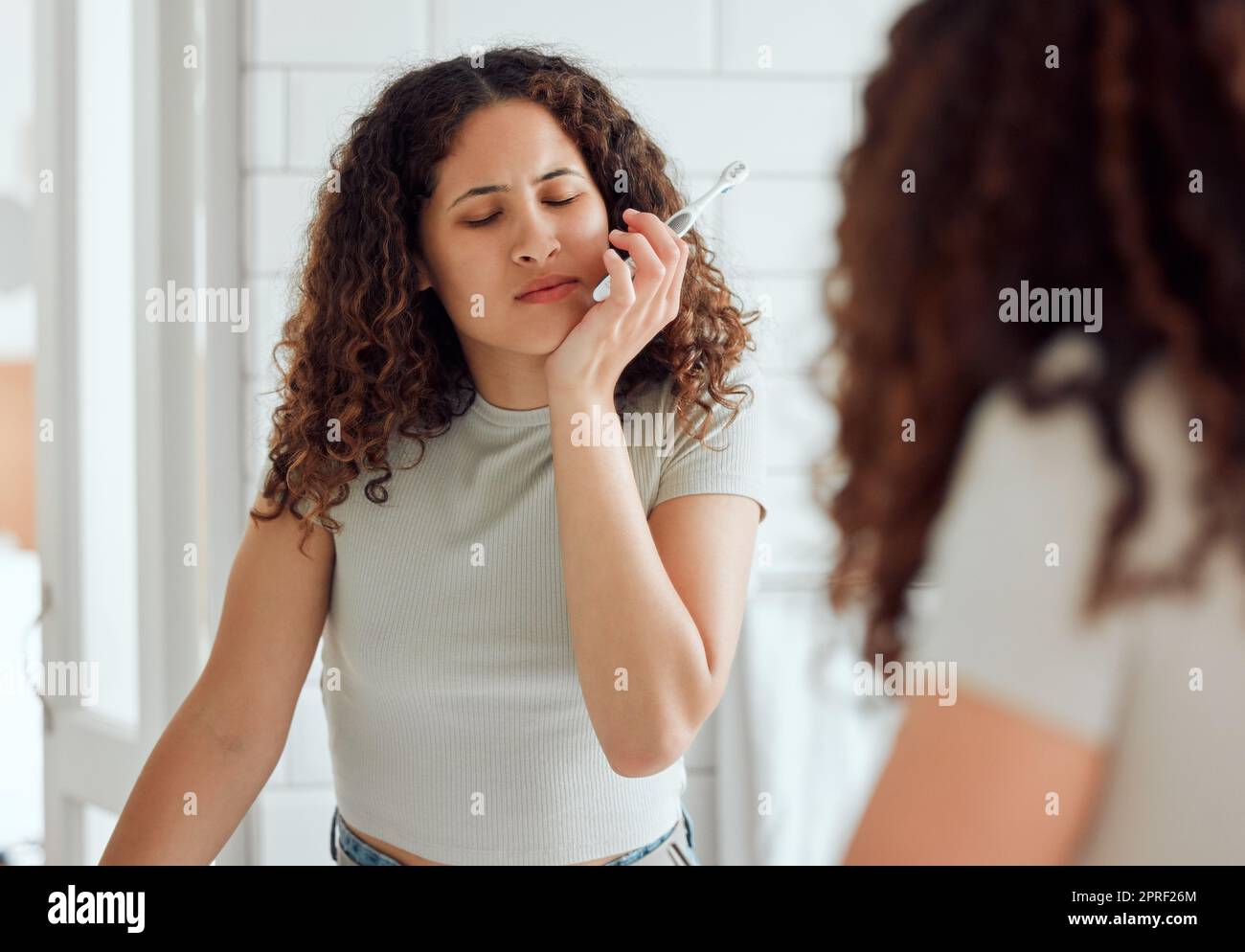 Toothache, oral pain and dental sensitivity for a woman brushing her teeth in the morning. African American female suffering with a painful, hurting or inflammation in her mouth in the bathroom Stock Photo
