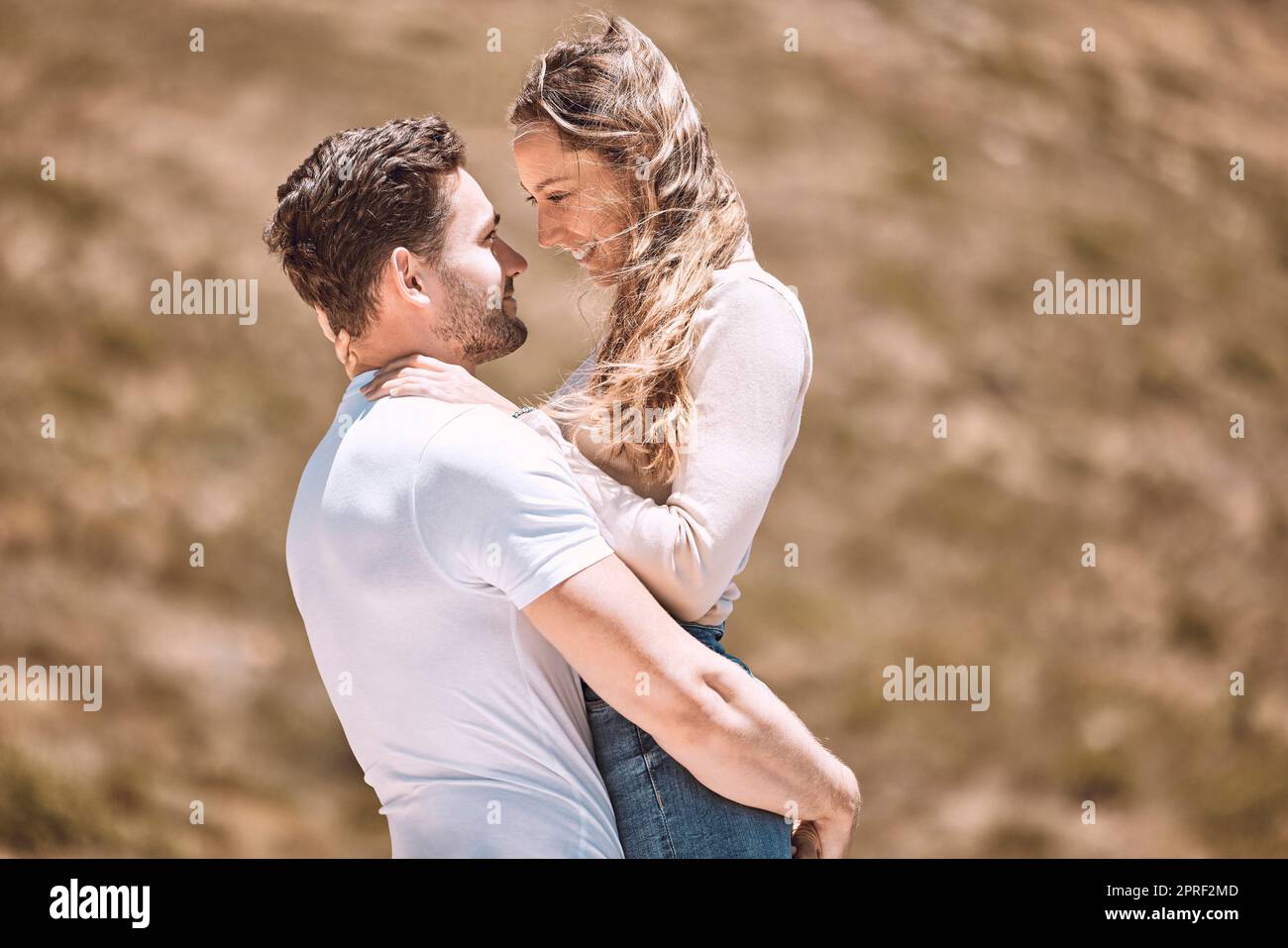 A young loving, affectionate and caring couple bonding while enjoying the day outdoors in nature. Happy, in love and smiling man embracing his wife wh Stock Photo