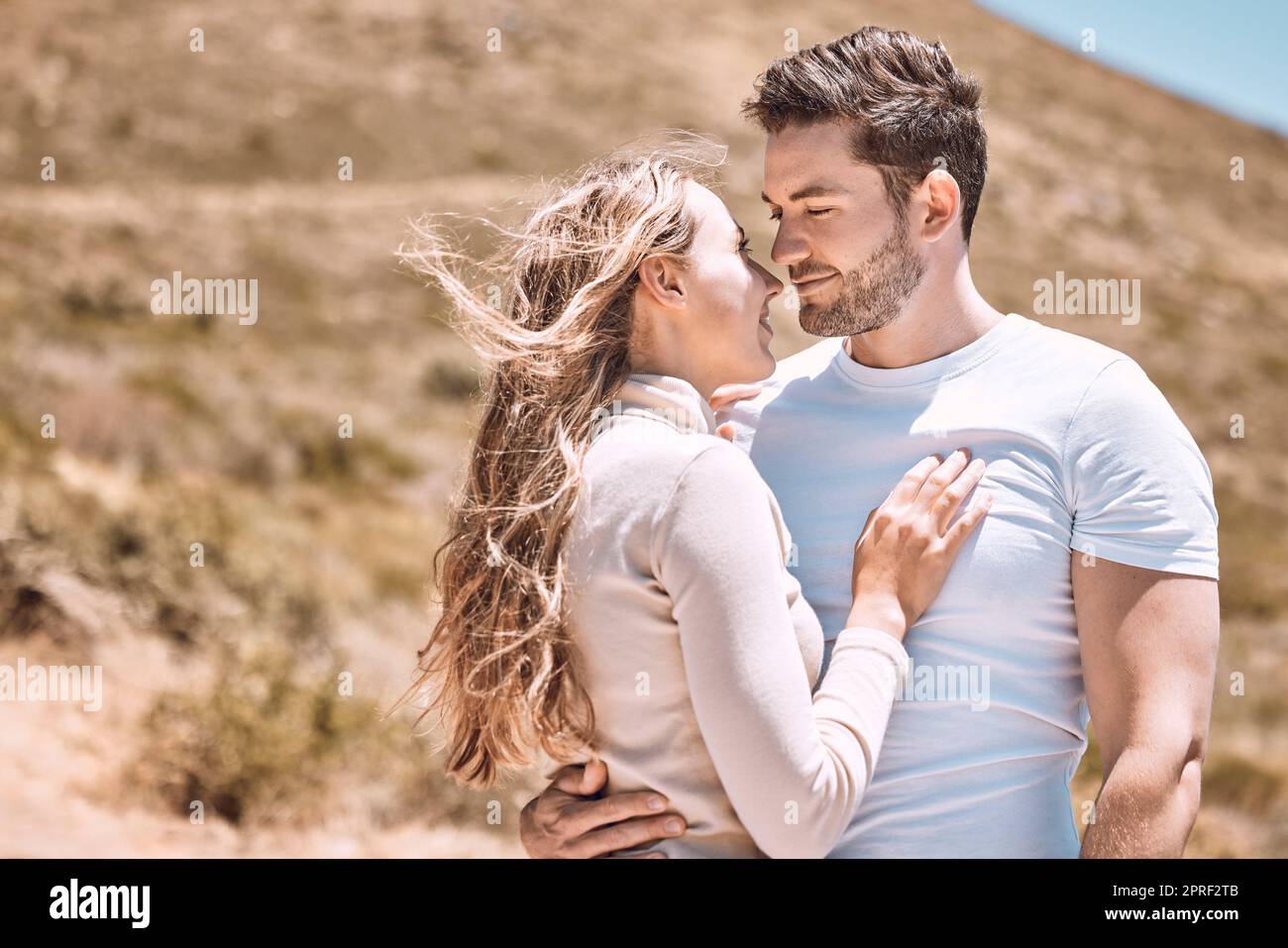 In love, hugging and bonding young couple happy, smiling on an outdoors vacation getaway. Romantic couple relax outside together embracing and loving romance, happiness and the sun on a summer day Stock Photo