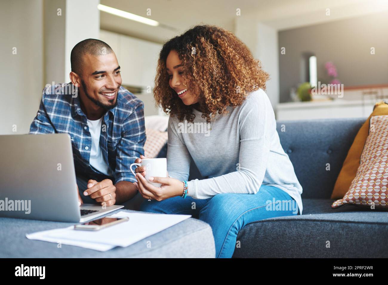 Babe, you buy too many shoes. a happy young couple sitting on the sofa together in their living room and using their laptop. Stock Photo