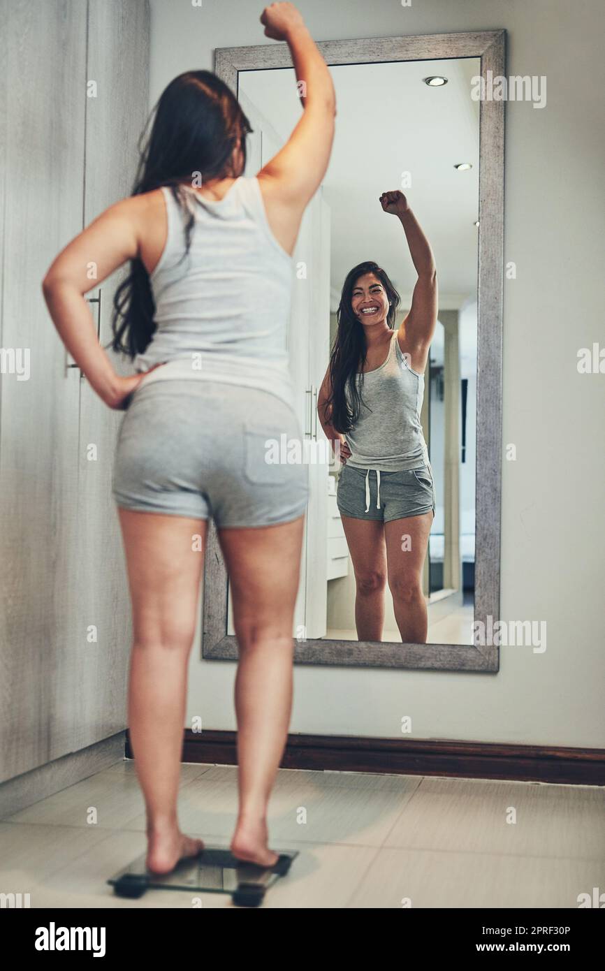 Ive finally hit the number Ive been aiming for. a young woman cheering while weighing herself on a scale at home. Stock Photo