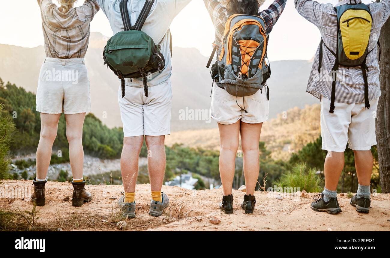 . Fitness group celebrating on hike in nature, enjoying hiking view on a mountain on a wellness getaway vacation together. Back of friends walking on weekend and relaxing on summer holiday. Stock Photo