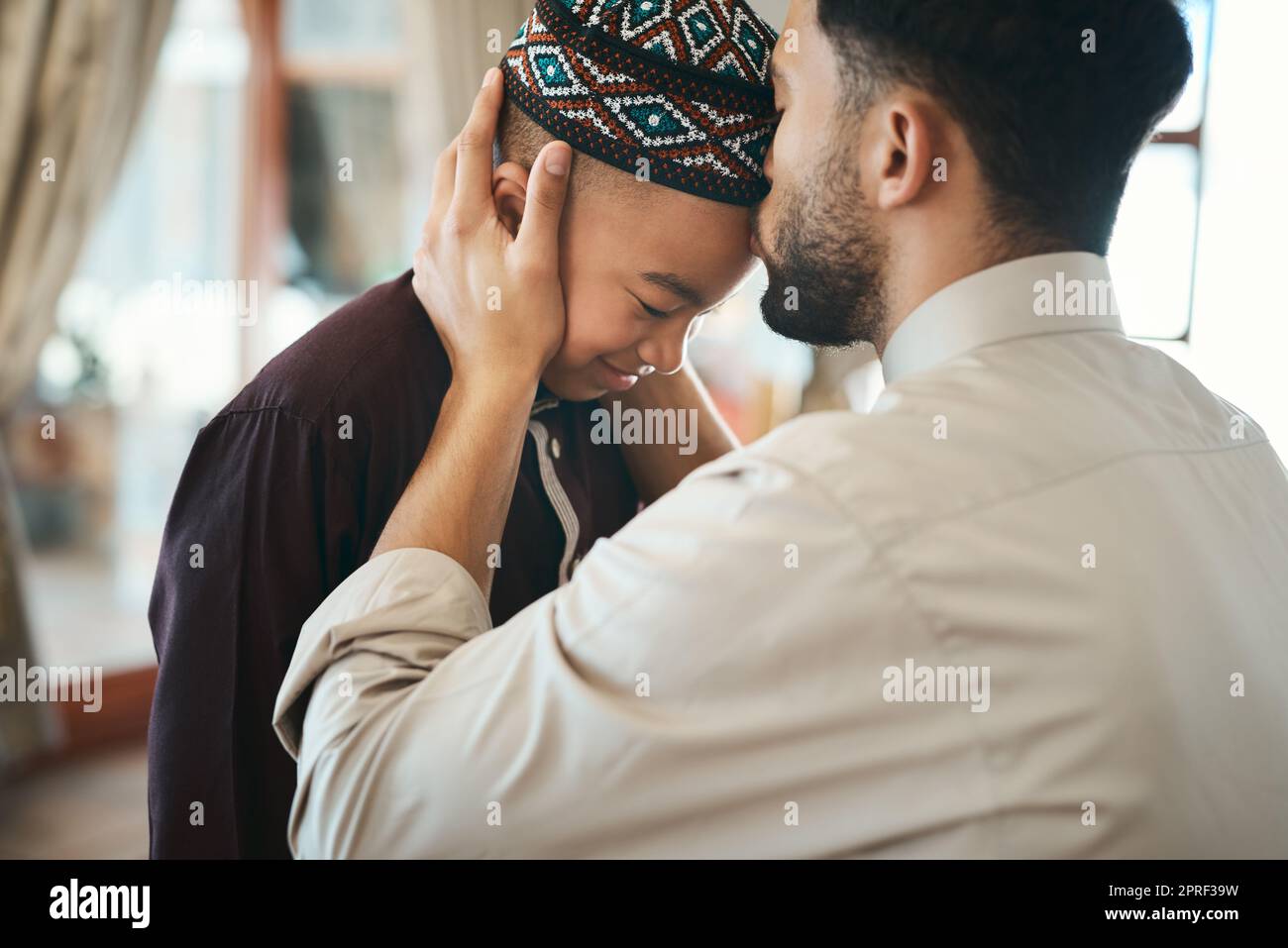 Muslim father, parent or man kissing his son on the forehead, bonding and showing affection at home. Happy, smiling and Arab boy embracing, celebrating traditional holiday and being peaceful with dad Stock Photo