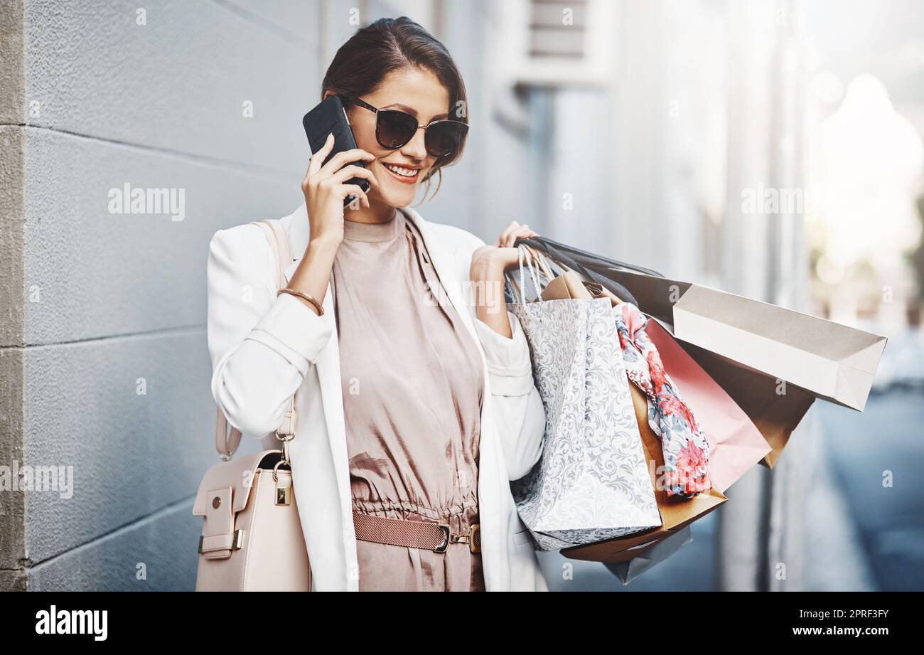 Trendy, stylish and fashionable woman shopping, purchasing and buying clothes in city, town and downtown. Elegant lady talking on phone with gift bags, going on spending spree or doing retail therapy Stock Photo