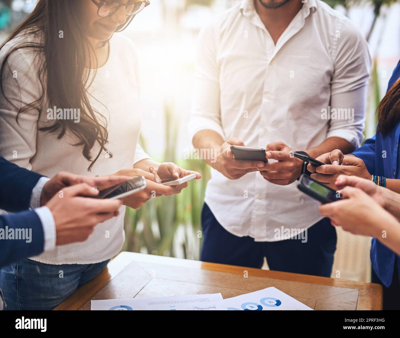 We are in a age of communication. a group of unrecognisable work colleagues standing in a circle and using their cellphones. Stock Photo