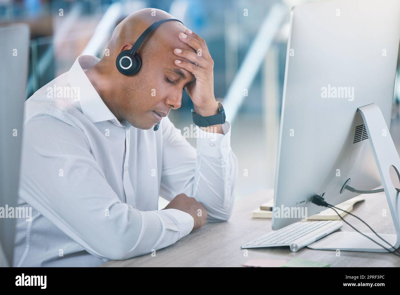 Stressed, tired and headache of working sales consultant, call center agent or customer service advisor. Overworked, worried or frustrated phone operator employee at contact us helpdesk agency Stock Photo