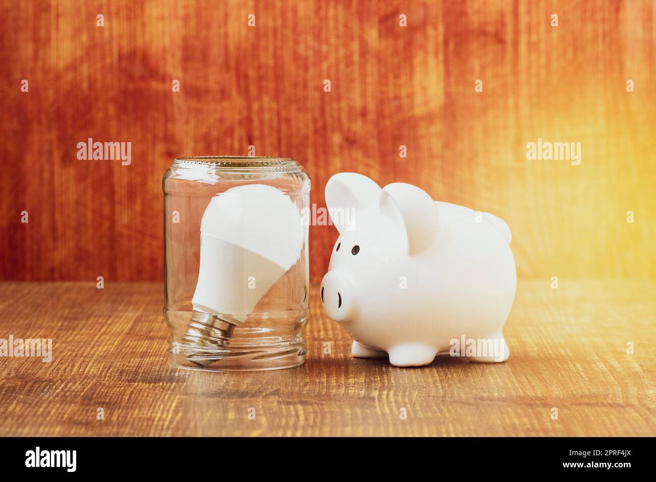 Piggy bank standing next to light bulb inside glass jar Stock Photo