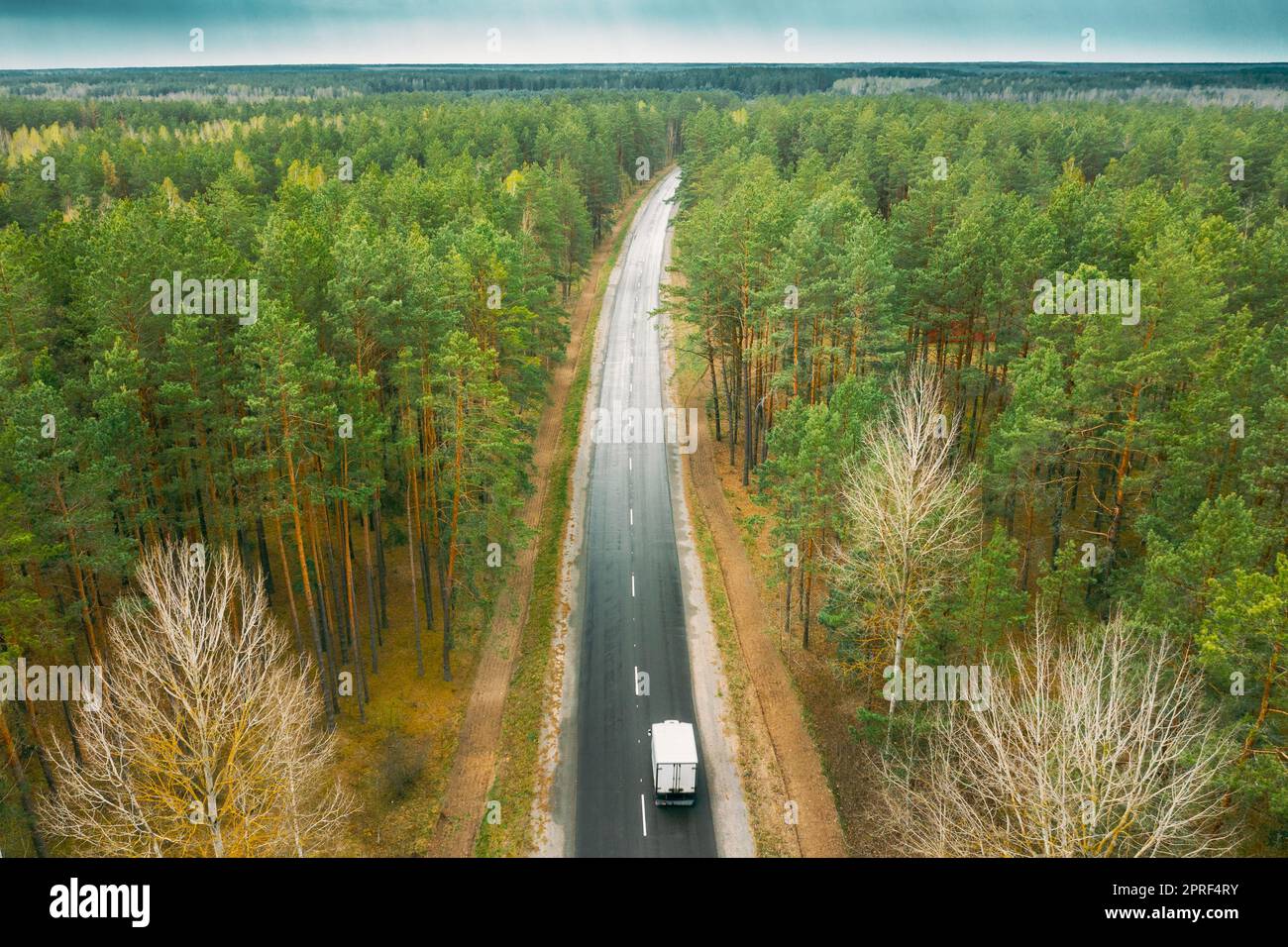 Aerial View Of Highway Road Through Spring Forest Landscape. Top View Of Truck Tractor Unit Prime Mover Traction Unit In Motion On Freeway. Business Transportation, Trucking Industry Stock Photo