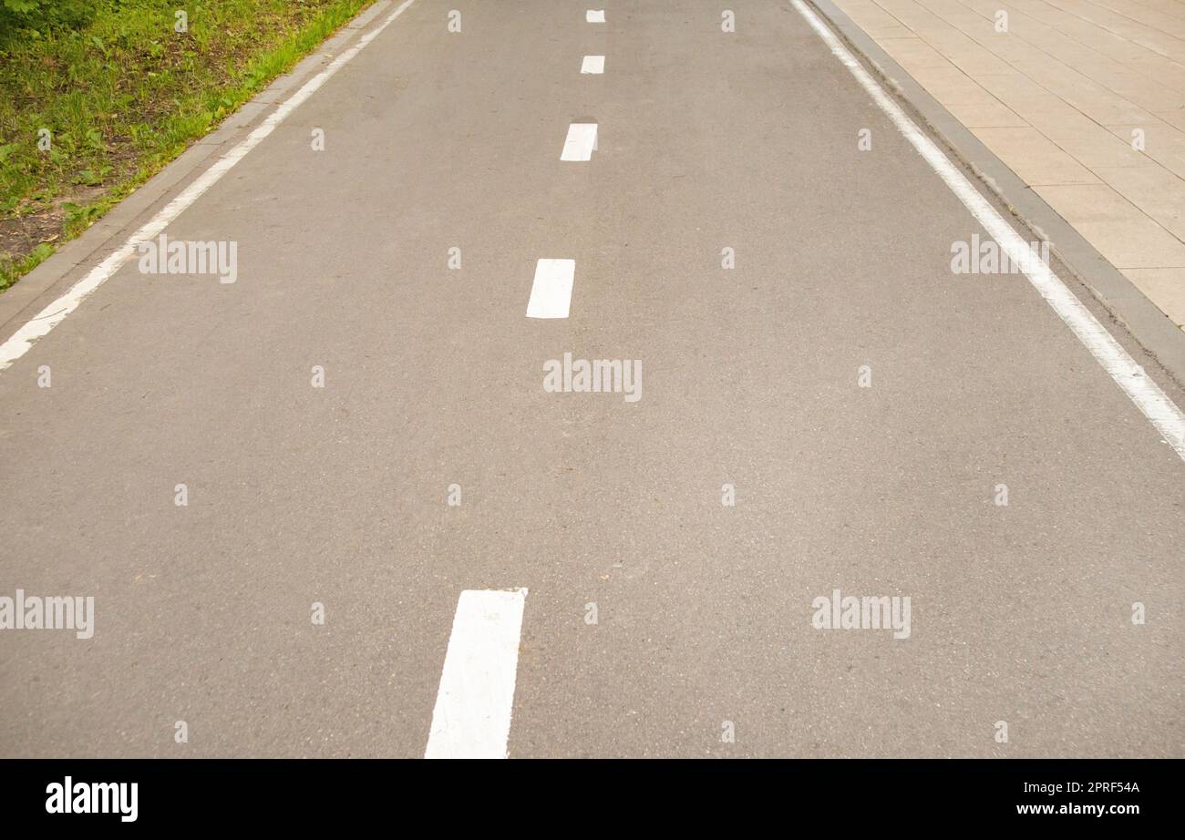 Close-up of an asphalt road with an intermittent marking line and grass on the side of the road. Selective focus, black and white photography Stock Photo