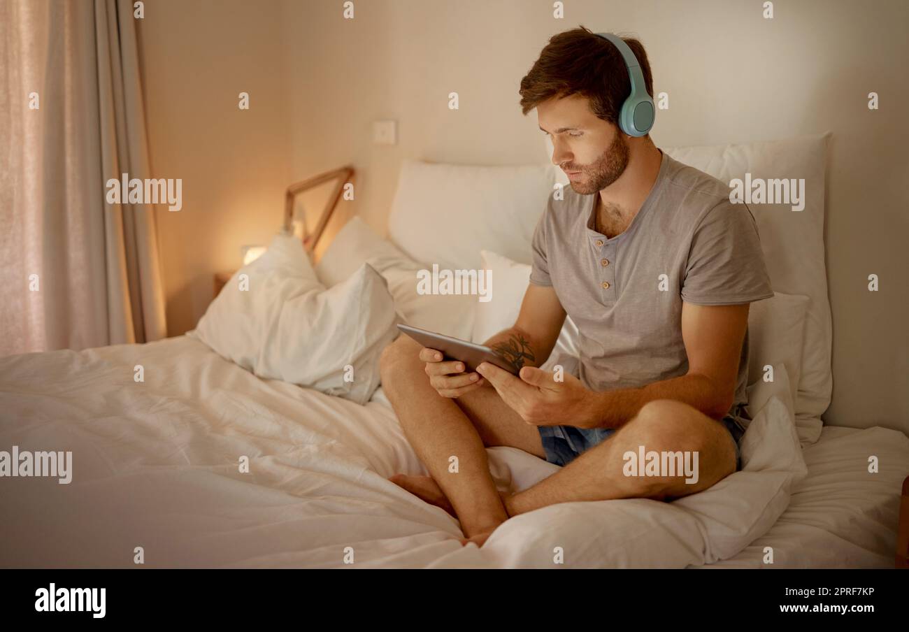 Headphones, digital tablet and in bed watching online movies, videos or series at night in house bedroom. Man on entertainment news or internet film streaming app or website on home 5g wifi network Stock Photo