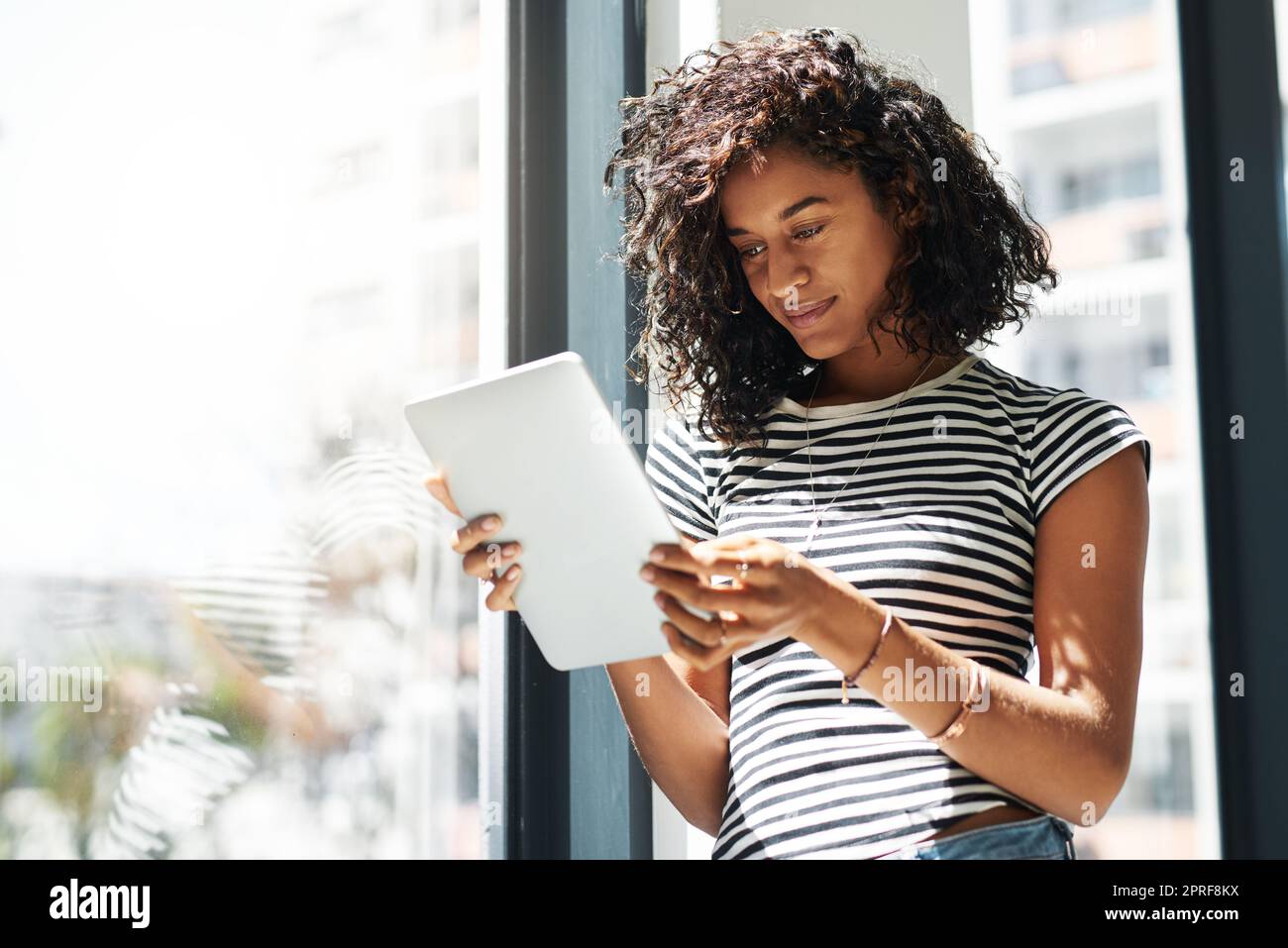 Checking my emails. an attractive young businesswoman standing alone in her home and using a tablet. Stock Photo