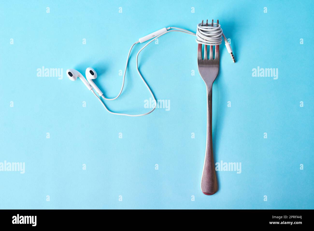 Music is the nourishment of life. Studio shot of earphones wrapped around a fork against a blue background. Stock Photo