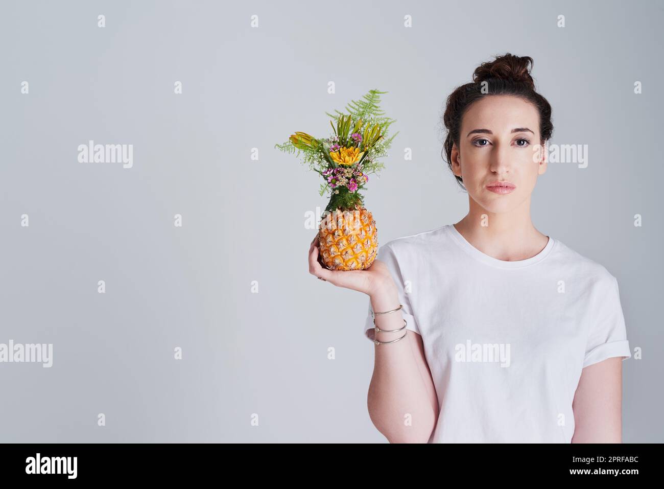 Thats one fineapple you holding there. Studio shot of a beautiful young woman holding a pineapple against a grey background. Stock Photo