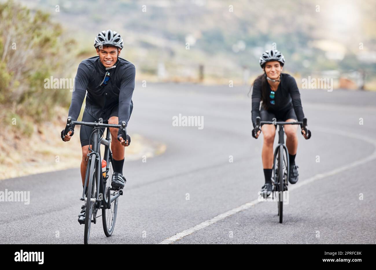 Cycling, couple goals and fitness while riding bicycle on countryside road for health and exercise. Happy male and female cyclists and athletes looking happy while training for sports race or hobby Stock Photo