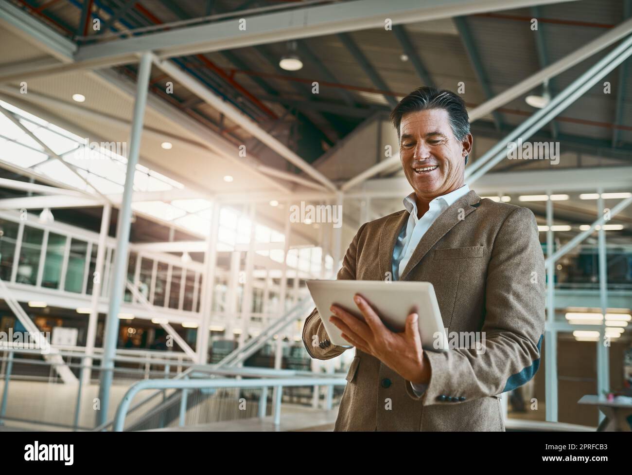 happy boss happy business. a mature businessman standing in the office and making notes on his tablet for the business. Stock Photo