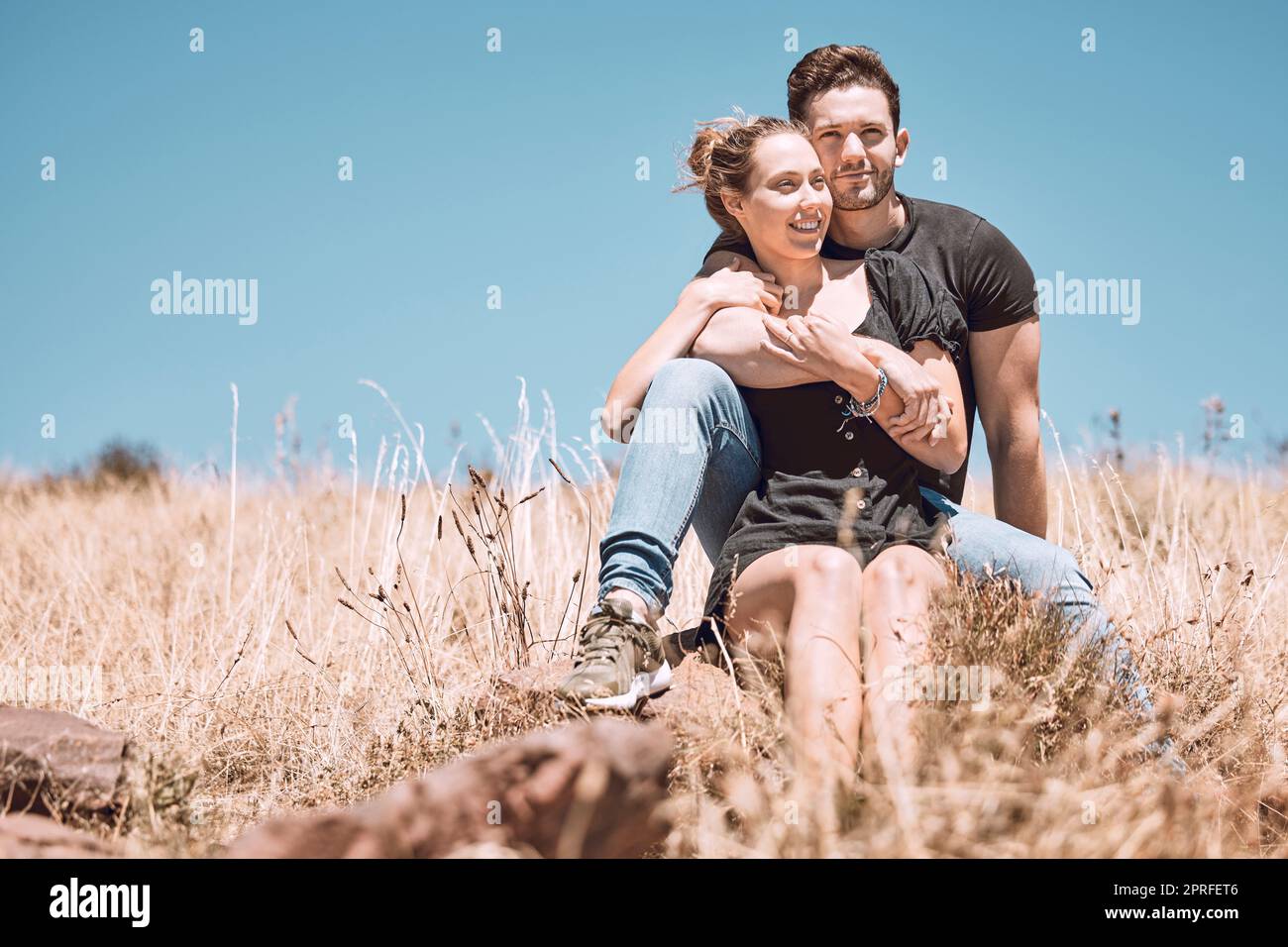 Carefree, smiling and relaxed couple bonding, having fun and looking at the view while sitting on the grass in a nature park together. Loving, caring and romantic boyfriend and girlfriend hugging Stock Photo