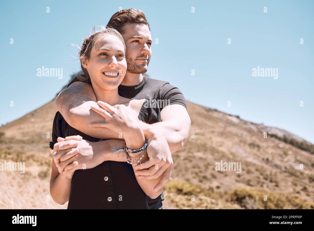 Love, romance and dating with an affectionate young couple bonding while enjoying hiking, adventure and exploring together. Hugging, loving and dating with a man and woman looking at a nature view Stock Photo