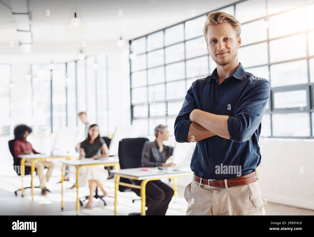 Let my winning team help you design your best future. Portrait of a happy designer posing in the office while his colleagues work in the background. Stock Photo