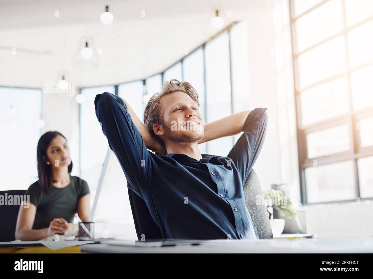 You cant help but smile when everything goes your way. a contented designer leaning back in his chair in a modern office. Stock Photo