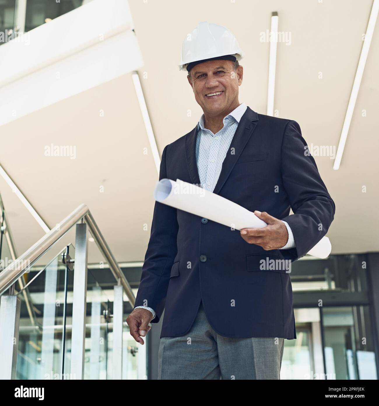 Without him there will be no development. Portrait of a cheerful professional male architect looking at the camera while holding blueprints inside a building. Stock Photo