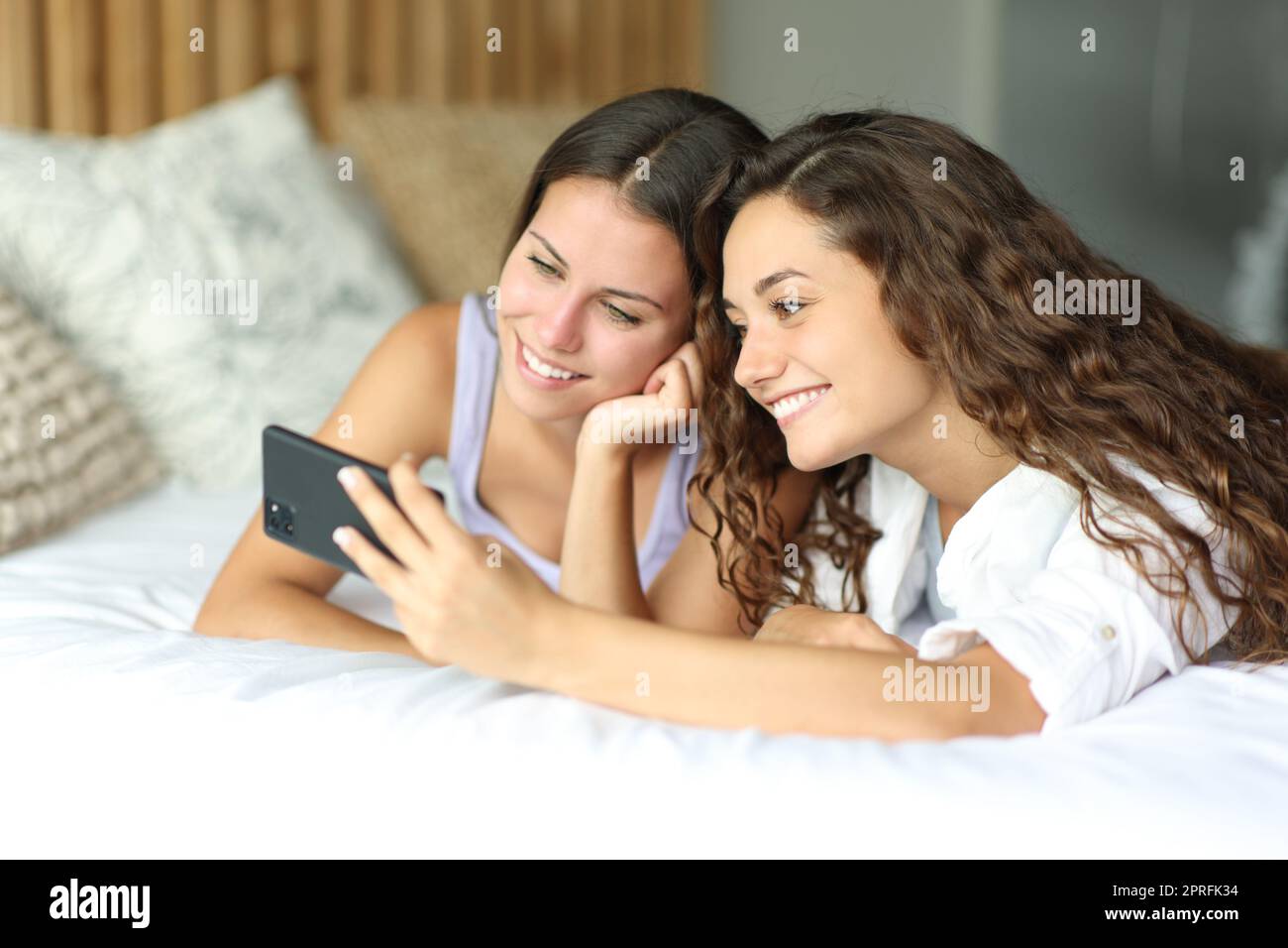 Two friends checking phone on a hotel bed Stock Photo