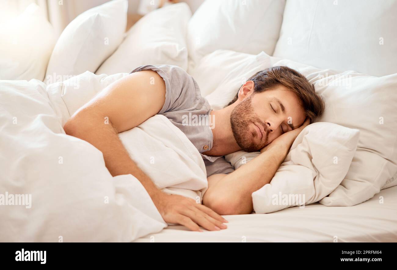 Relax, sleep and peace of a tired man sleeping in a bedroom bed at home. Dreaming, relaxing and resting calm attractive person with closed eyes on a pillow at his house in the morning taking a nap Stock Photo