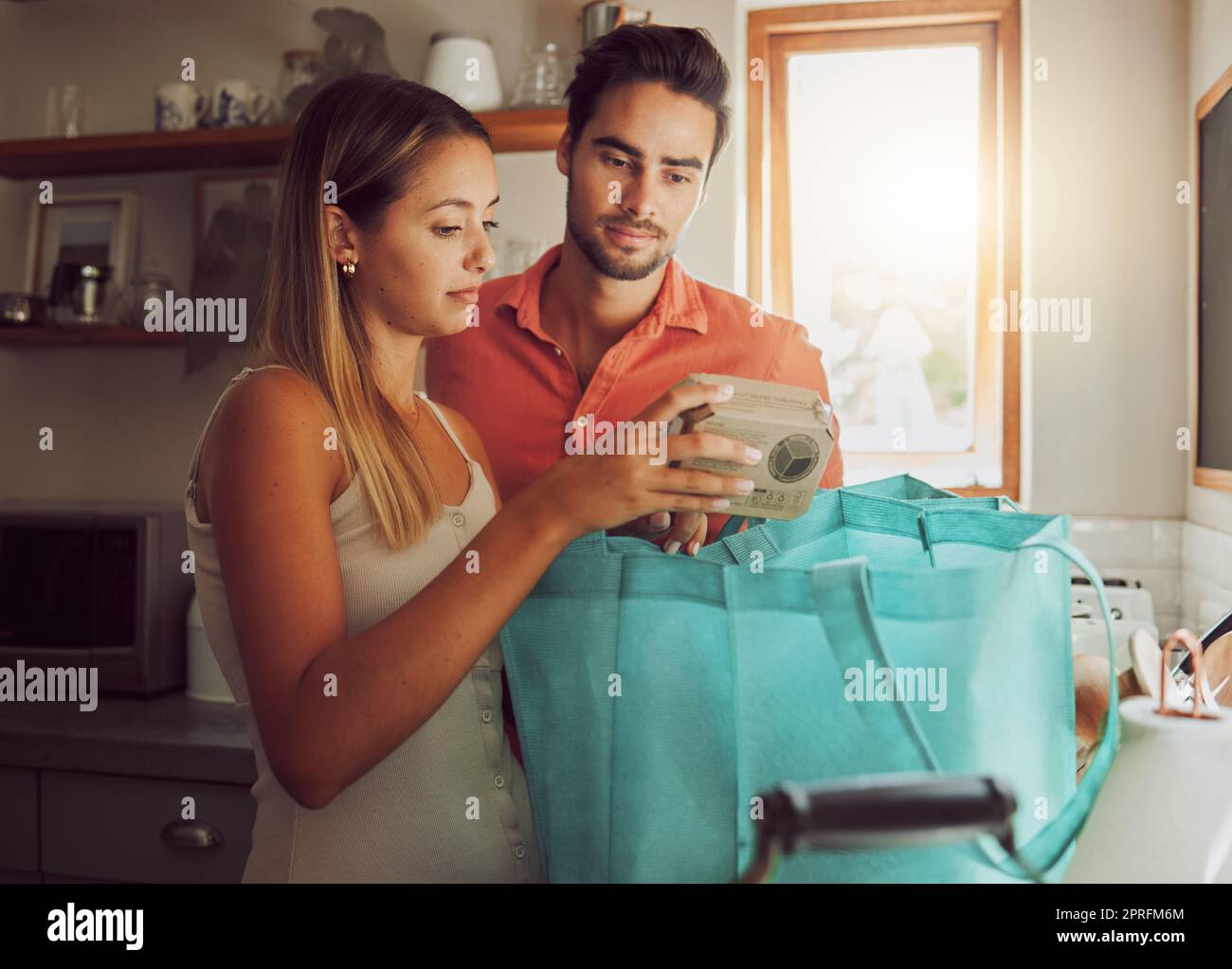 Wrong order of grocery, food and kitchen products bought by a couple for home cook dinner or lunch. Unhappy male and female unpacking diet cooking supplies, ingredients or groceries from shopping bag Stock Photo