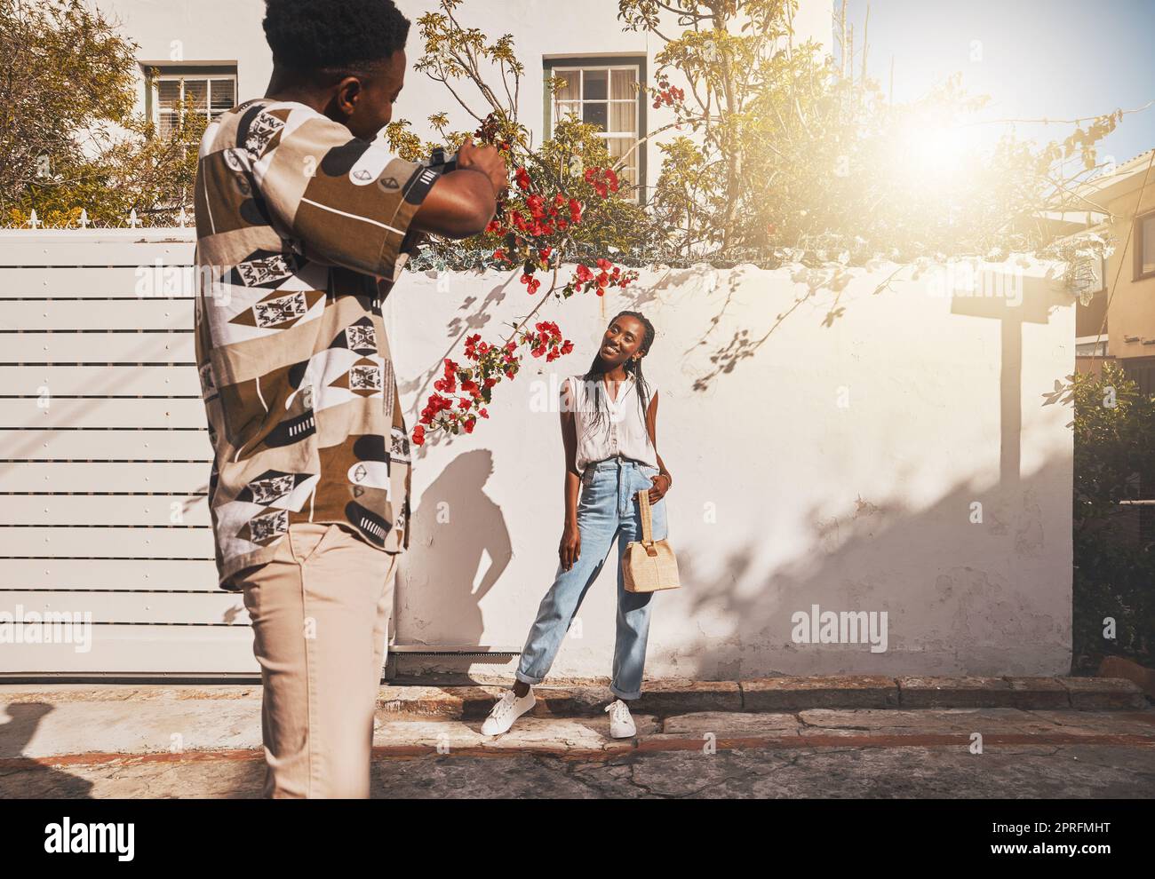 Photographer with model for summer fashion photography taking photo, posing and smiling for portrait shot with lens flare. African creative freelancer taking picture of young influencer woman outside Stock Photo