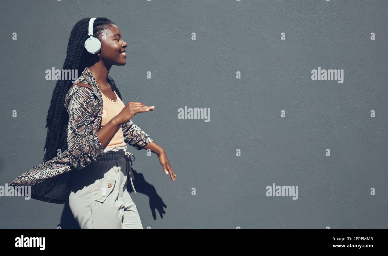 Music, university and college dance student dancing and listening to podcast or radio on headphone walking past campus. Copy space banner for education mock up content on grey wall background. Stock Photo