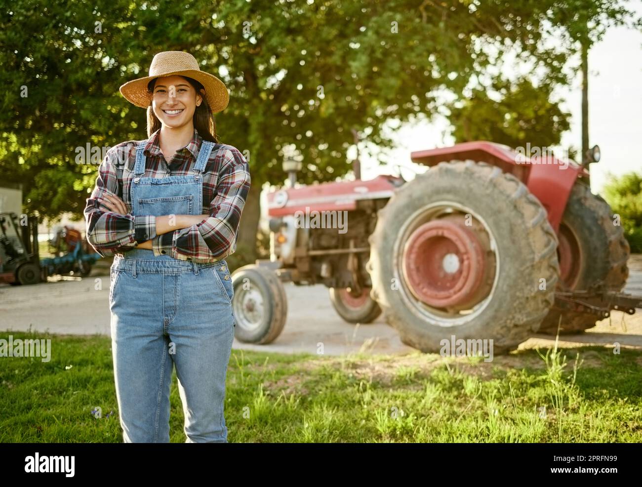 Farm, agriculture and tractor with a young woman farmer standing outside in the farming industry. Sustainability, organic and eco friendly agricultural harvest during summer or spring harvest season Stock Photo