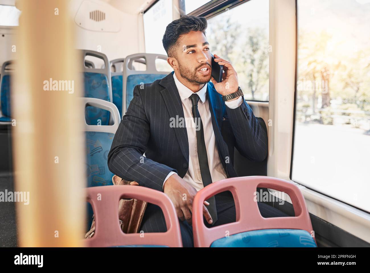 Businessman consulting on a phone call on a bus in the morning travel to work in the city. Entrepreneur, employee and worker speaking to a contact on a mobile cellphone in public transportation Stock Photo