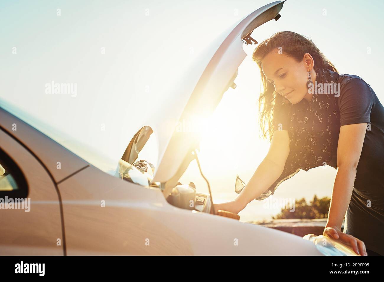 Shes got some mechanical difficulties with her car. a young woman checking under the hood of her car after breaking down on the roadside. Stock Photo
