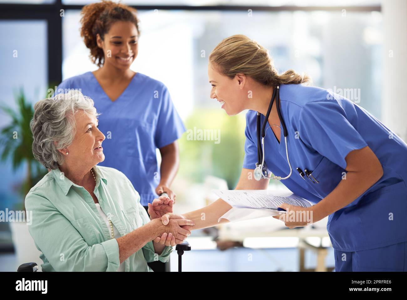 Lets get you admitted. a doctor holding medical records and shaking hands with a smiling senior woman sitting in a wheelchair. Stock Photo