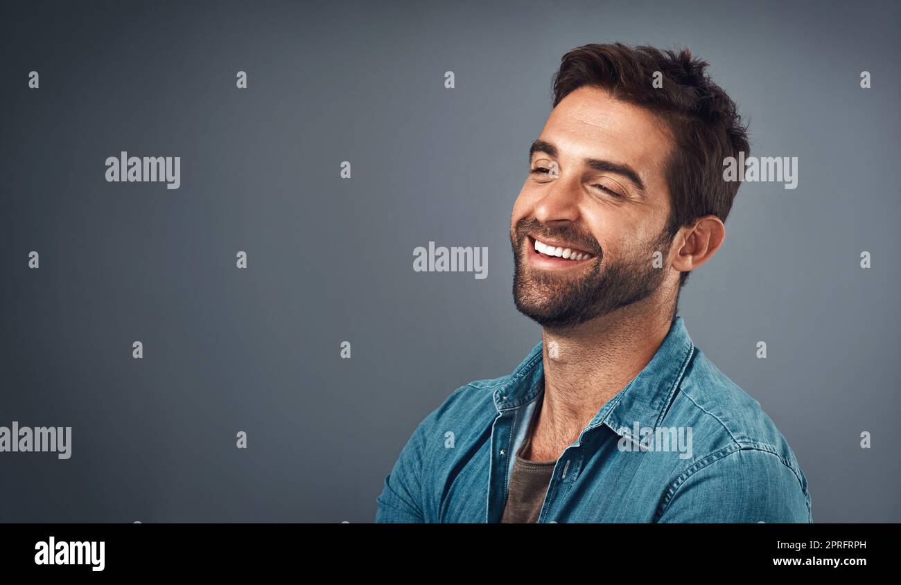 Laughter adds so much to the day. Studio shot of a handsome and happy young man posing against a grey background. Stock Photo